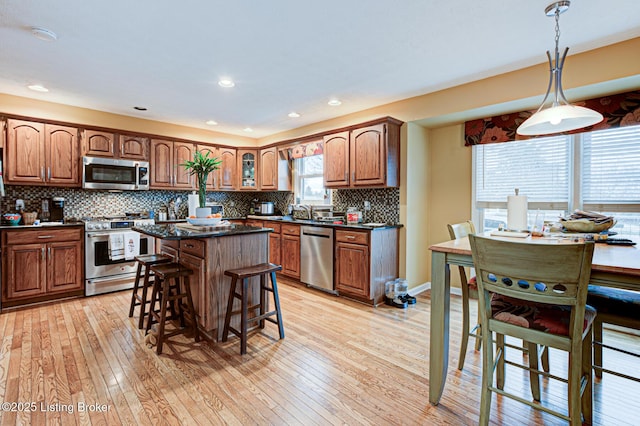 kitchen featuring light wood finished floors, decorative backsplash, dark countertops, appliances with stainless steel finishes, and a kitchen bar