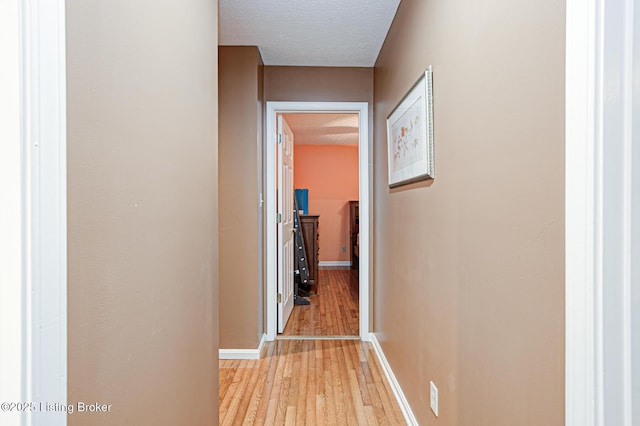 corridor with baseboards, a textured ceiling, and light wood finished floors