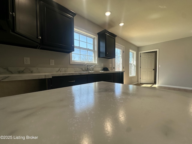 kitchen with light countertops, dark cabinetry, baseboards, and a sink