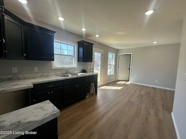 kitchen with dark cabinetry, light stone countertops, baseboards, light wood-style flooring, and a sink