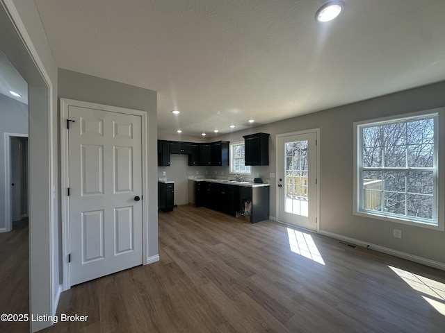 kitchen featuring baseboards, wood finished floors, visible vents, and dark cabinets