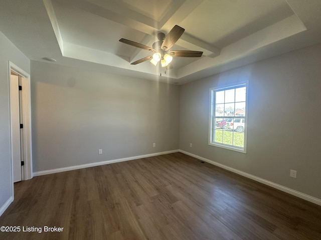 empty room featuring visible vents, a raised ceiling, dark wood-style floors, baseboards, and ceiling fan