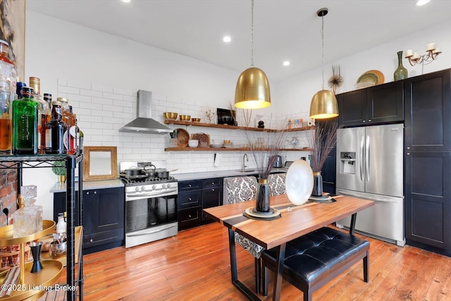 kitchen with stainless steel appliances, dark cabinetry, wall chimney exhaust hood, light wood finished floors, and tasteful backsplash