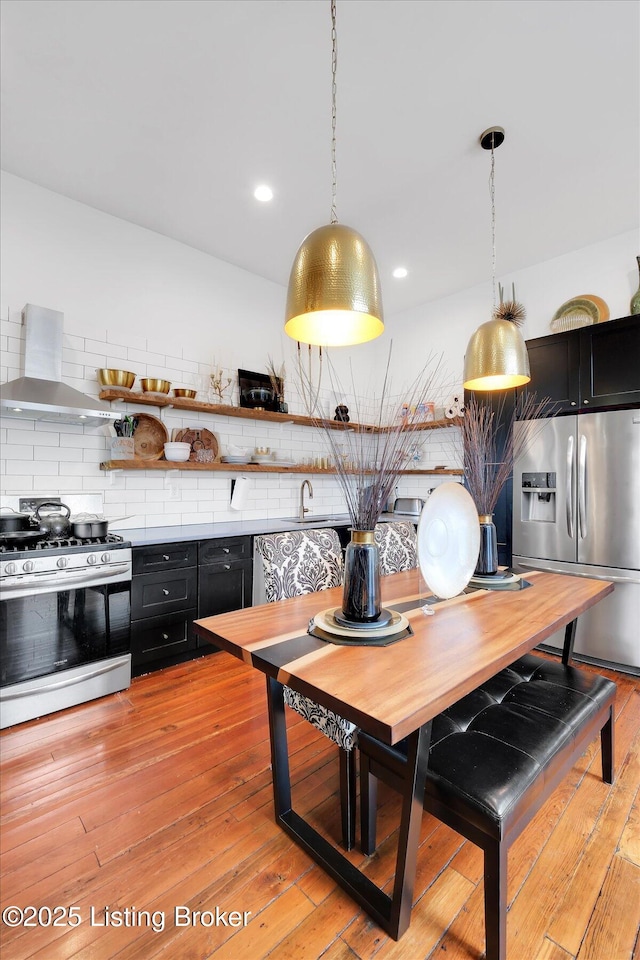 kitchen featuring stainless steel appliances, dark cabinetry, wall chimney exhaust hood, and tasteful backsplash