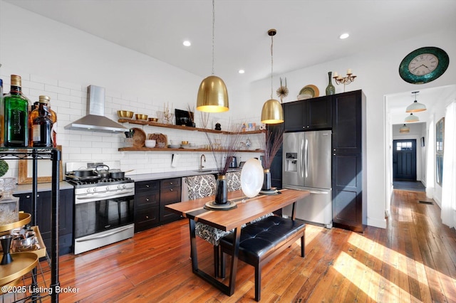 kitchen featuring stainless steel appliances, open shelves, decorative backsplash, wall chimney exhaust hood, and light wood finished floors