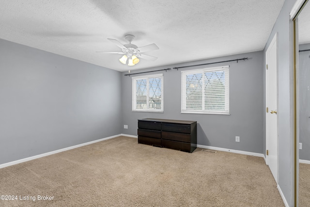 carpeted empty room featuring a textured ceiling, baseboards, and a ceiling fan