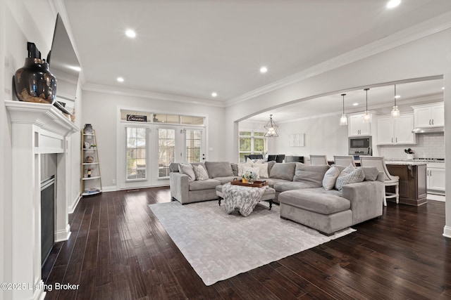 living area featuring a healthy amount of sunlight, arched walkways, dark wood finished floors, and crown molding