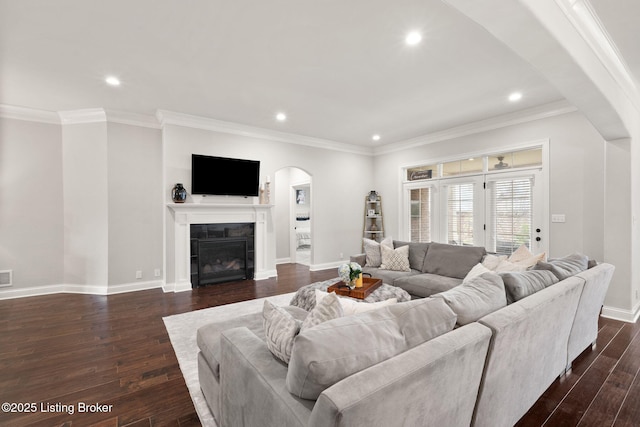 living room with arched walkways, dark wood-style flooring, a glass covered fireplace, and baseboards