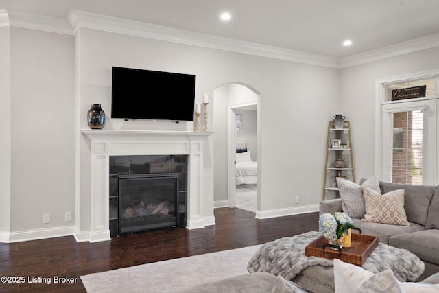 living area with baseboards, arched walkways, a tiled fireplace, wood finished floors, and crown molding