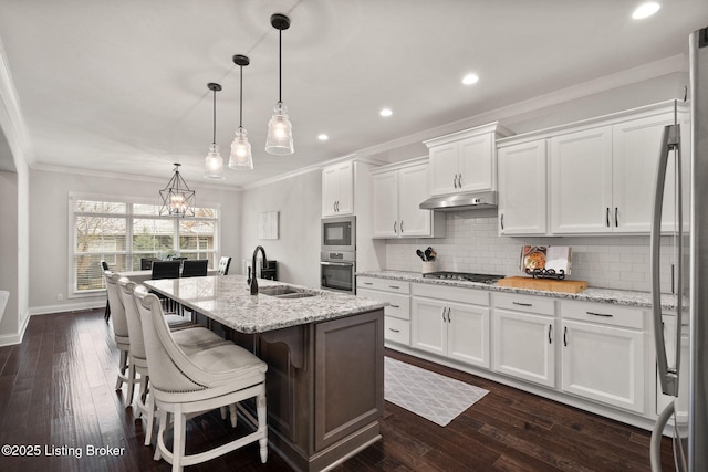 kitchen featuring under cabinet range hood, crown molding, white cabinetry, and a sink