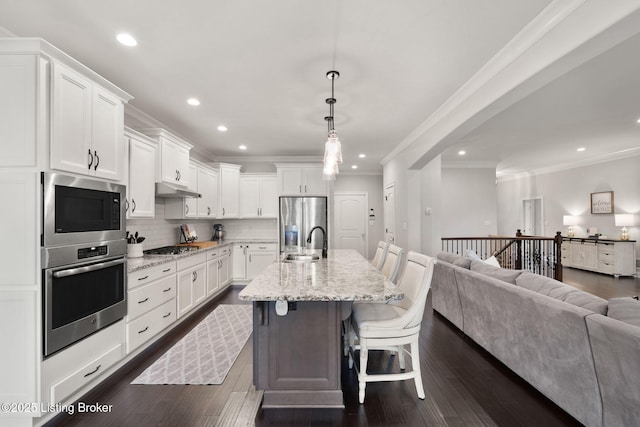 kitchen featuring under cabinet range hood, white cabinetry, open floor plan, appliances with stainless steel finishes, and decorative backsplash