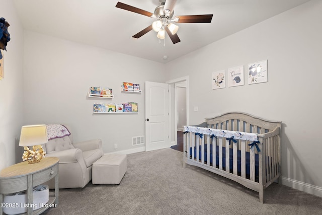 carpeted bedroom featuring a ceiling fan, visible vents, a crib, and baseboards