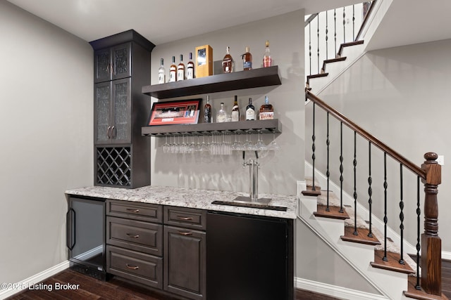 bar with dark wood-style floors, bar, baseboards, and stairs