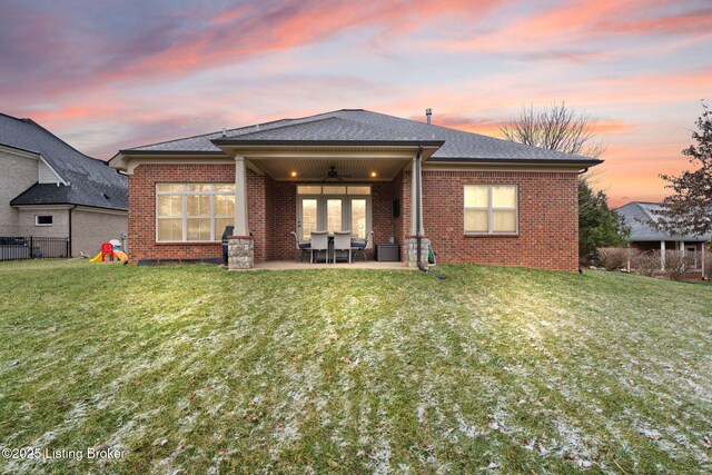 rear view of house with ceiling fan, a patio, brick siding, and a lawn