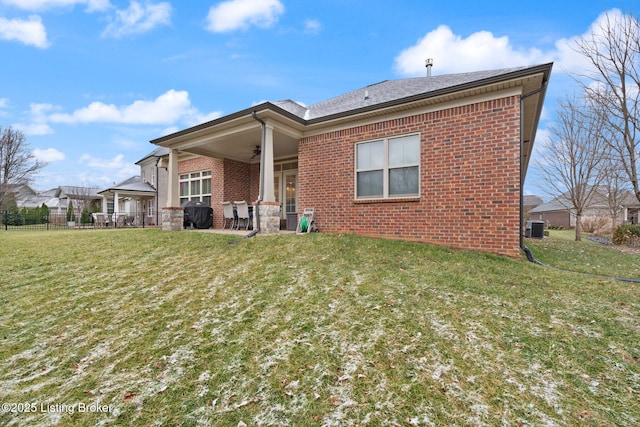 rear view of property featuring brick siding, a lawn, a ceiling fan, fence, and cooling unit