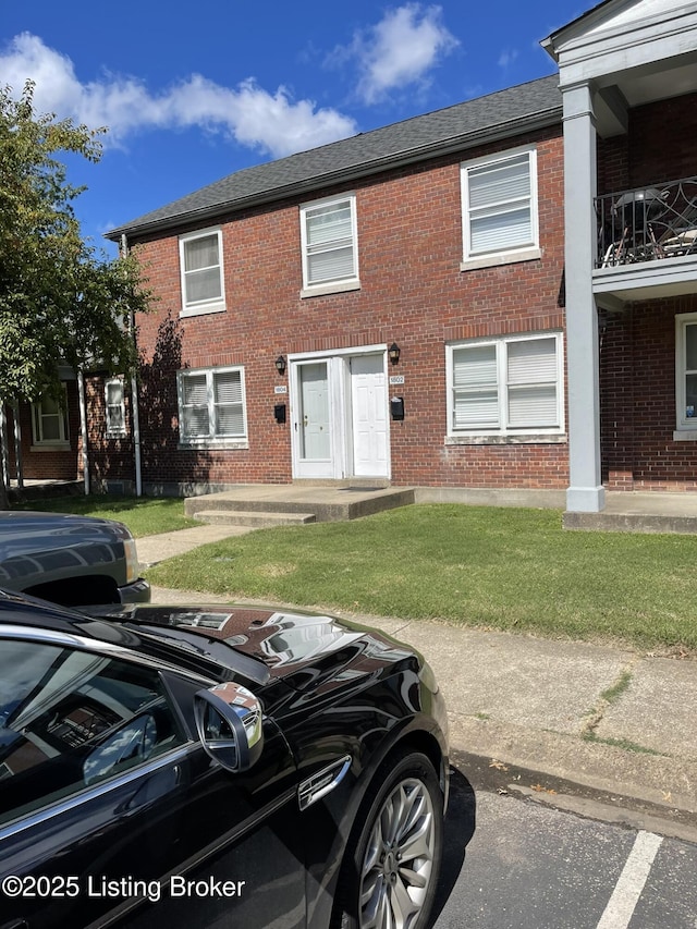 view of front of house featuring a front lawn, brick siding, and roof with shingles