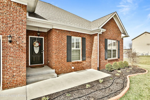 view of exterior entry featuring brick siding and roof with shingles