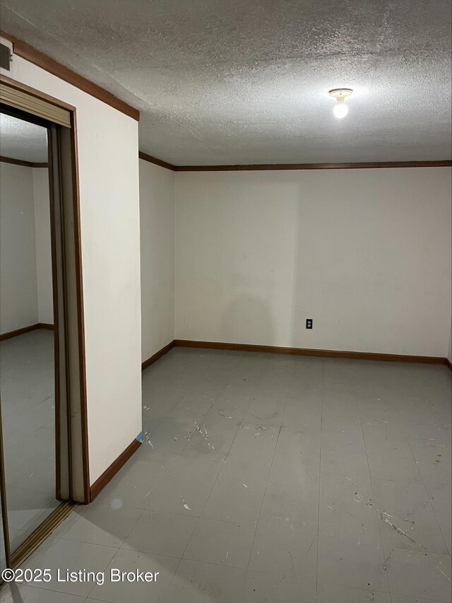 basement with a textured ceiling, crown molding, and baseboards