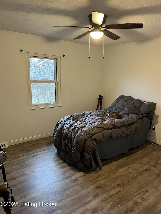 bedroom featuring visible vents, ceiling fan, baseboards, wood finished floors, and a textured ceiling