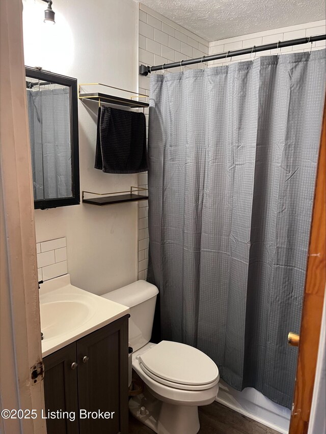 bathroom featuring toilet, curtained shower, a textured ceiling, and vanity