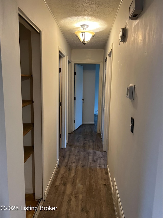 corridor featuring a textured ceiling, dark wood-type flooring, and baseboards