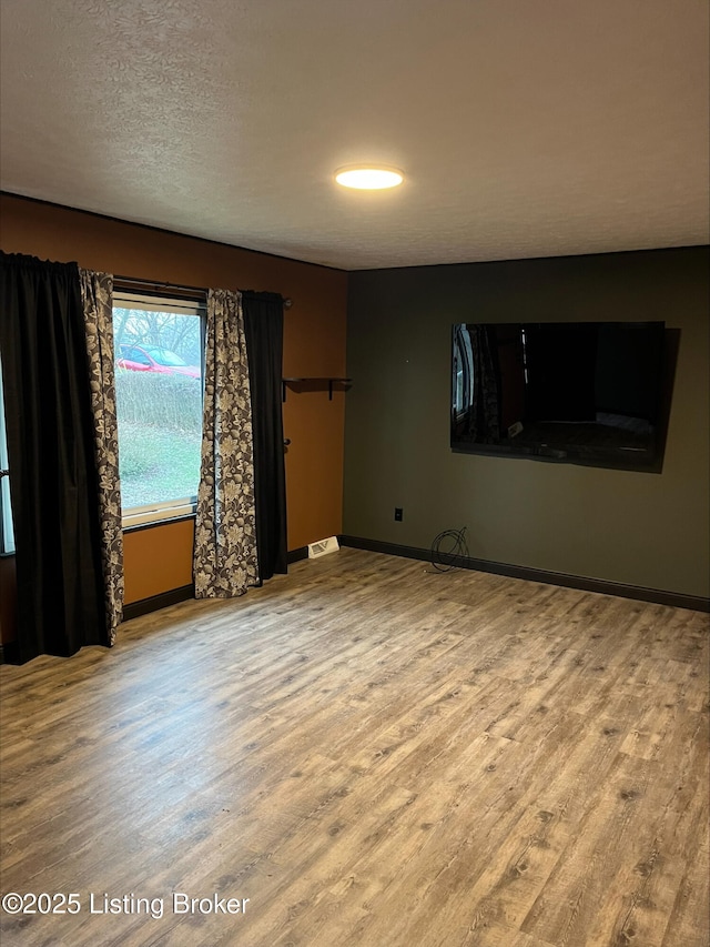 empty room with wood finished floors, baseboards, and a textured ceiling