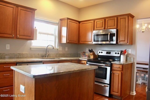 kitchen featuring a center island, brown cabinets, stainless steel appliances, a sink, and light stone countertops