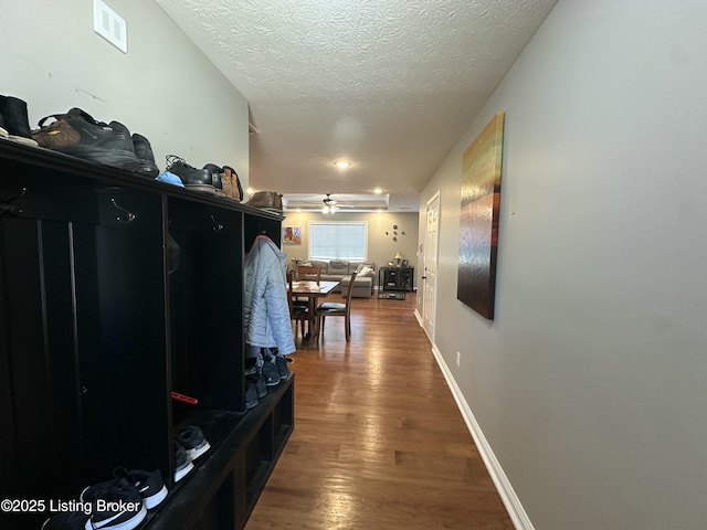 hall featuring visible vents, a textured ceiling, baseboards, and wood finished floors