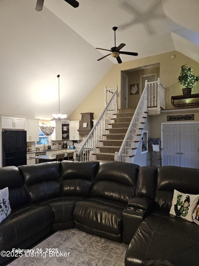 living room with stairs, high vaulted ceiling, and ceiling fan with notable chandelier