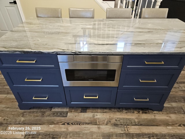 kitchen with blue cabinets, light stone countertops, dark wood-style floors, and wall oven