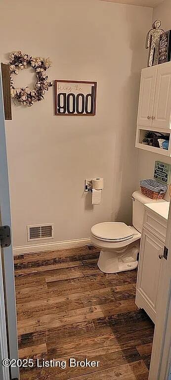 bathroom with baseboards, visible vents, toilet, and wood finished floors