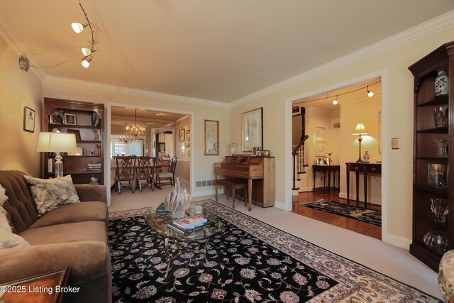 carpeted living area featuring crown molding, baseboards, stairs, rail lighting, and a notable chandelier