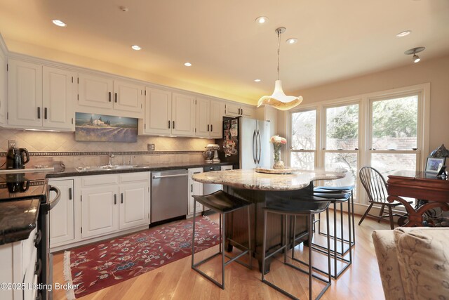 kitchen with a sink, a center island, white cabinetry, light wood-style floors, and appliances with stainless steel finishes