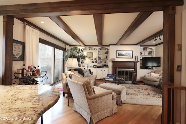 living area featuring beam ceiling, a fireplace with flush hearth, light wood-type flooring, and built in shelves