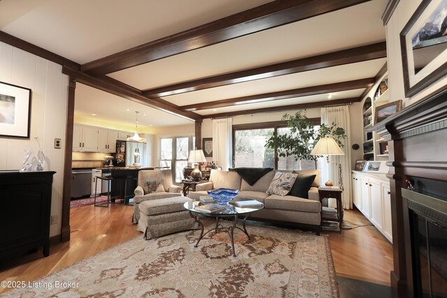 living room featuring beamed ceiling, wood finished floors, and a glass covered fireplace