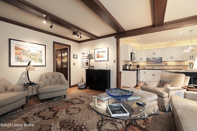 living area featuring beamed ceiling, ornamental molding, and wood finished floors