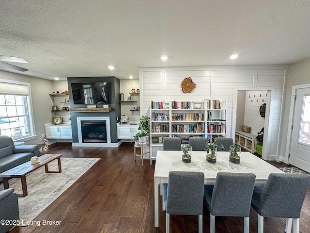 dining area with a textured ceiling, dark wood-style flooring, plenty of natural light, and a glass covered fireplace