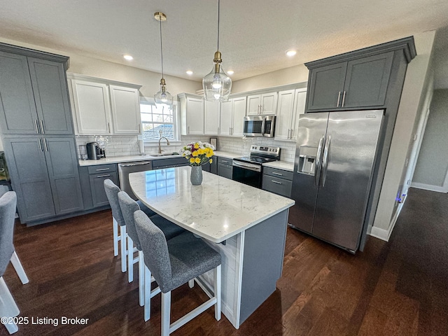 kitchen featuring dark wood finished floors, decorative backsplash, appliances with stainless steel finishes, a kitchen island, and a kitchen bar