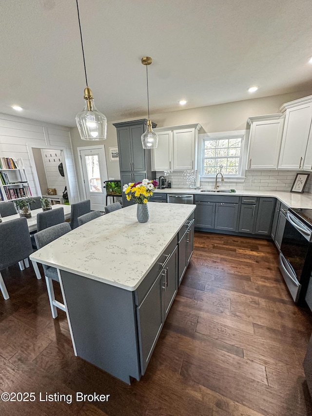 kitchen featuring gray cabinetry, electric range, a breakfast bar, a sink, and backsplash