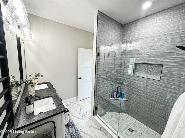 bathroom with marble finish floor, double vanity, a stall shower, a sink, and baseboards