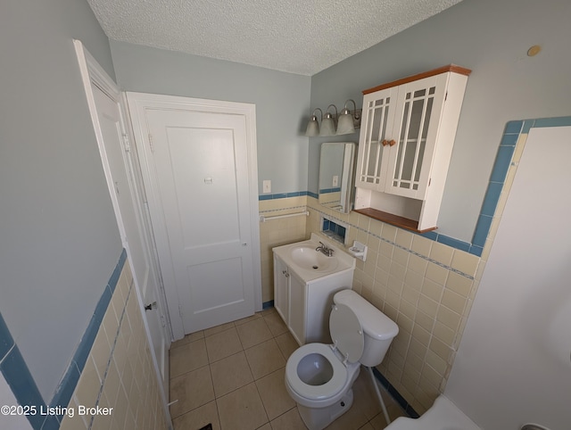 bathroom featuring tile patterned floors, a wainscoted wall, toilet, a textured ceiling, and tile walls