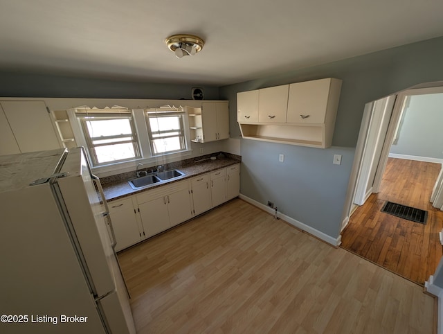 kitchen featuring a sink, open shelves, freestanding refrigerator, light wood-style floors, and white cabinets