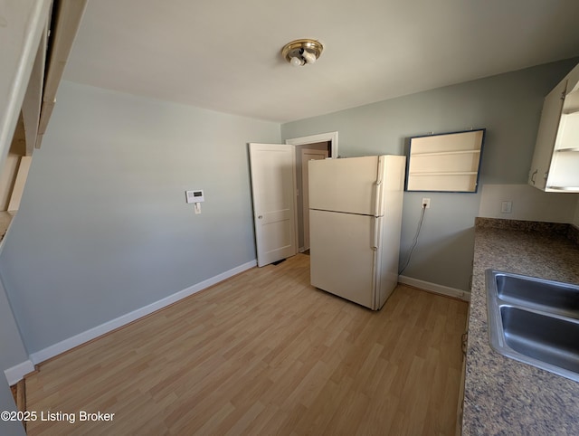 kitchen with baseboards, light wood-type flooring, freestanding refrigerator, and a sink