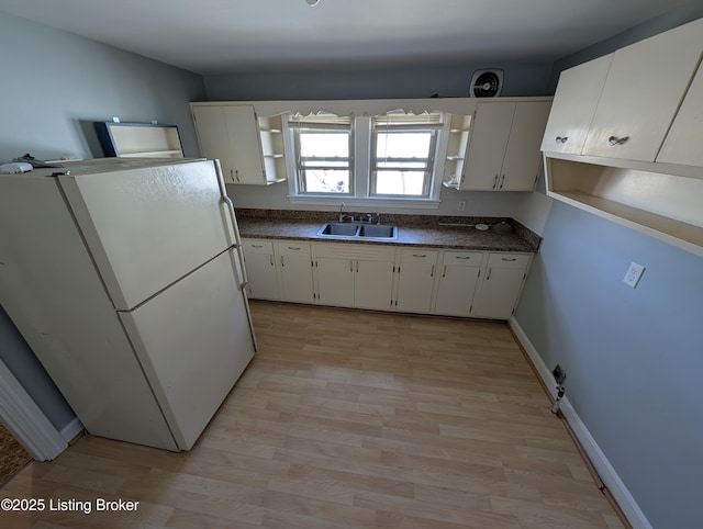 kitchen with dark countertops, open shelves, freestanding refrigerator, white cabinets, and a sink