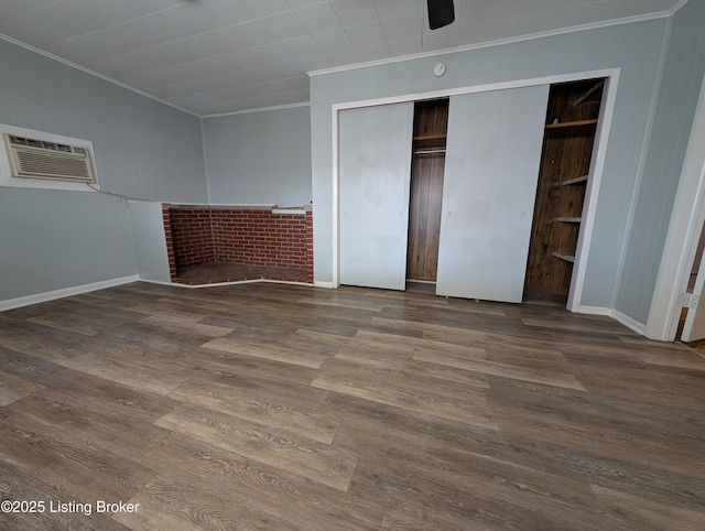 unfurnished bedroom featuring a wall mounted air conditioner, a closet, dark wood-style floors, and crown molding