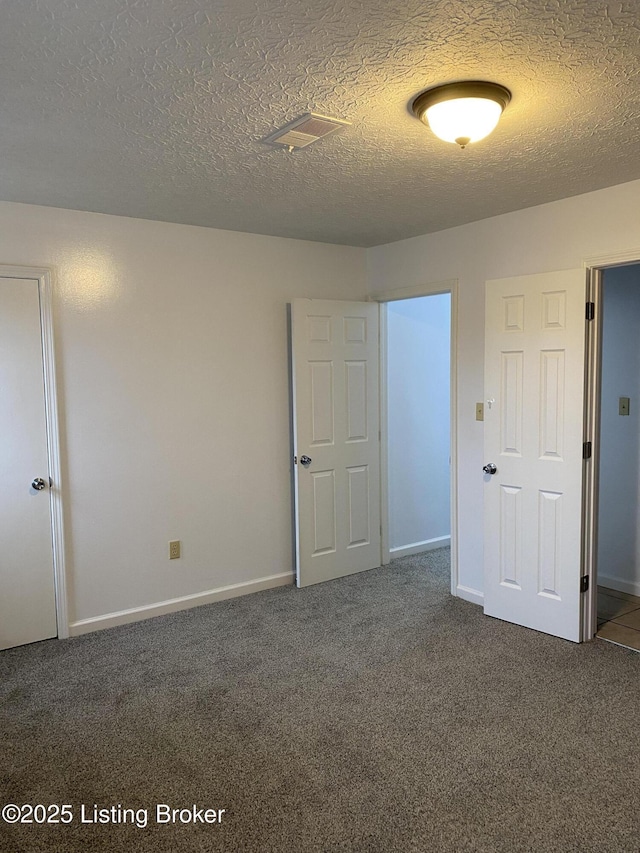 unfurnished bedroom with baseboards, a textured ceiling, and dark carpet