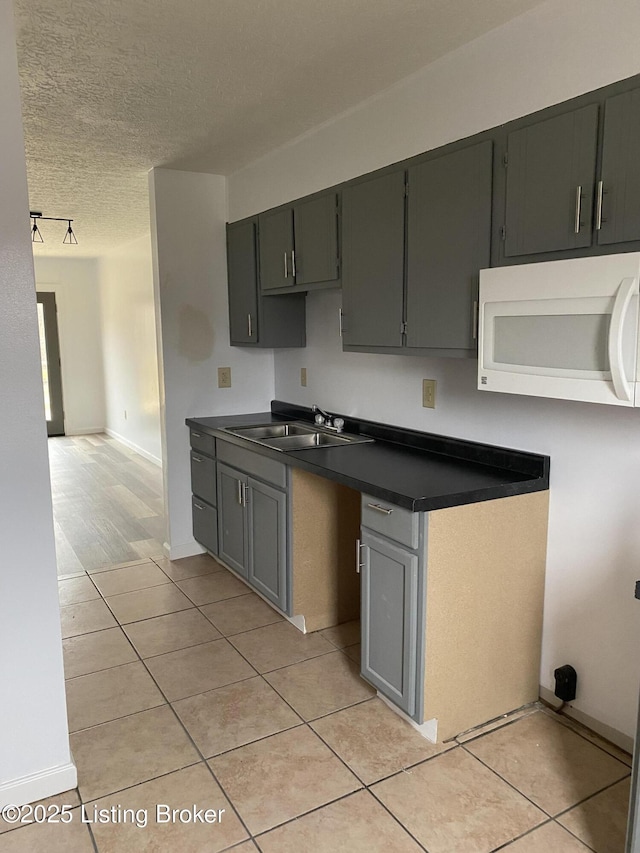 kitchen featuring white microwave, dark countertops, light tile patterned floors, a textured ceiling, and a sink