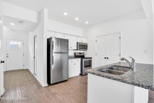 kitchen featuring light wood-style flooring, a sink, white cabinetry, appliances with stainless steel finishes, and dark stone countertops