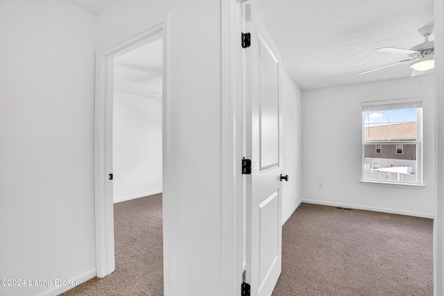 corridor with carpet floors, baseboards, and a textured ceiling