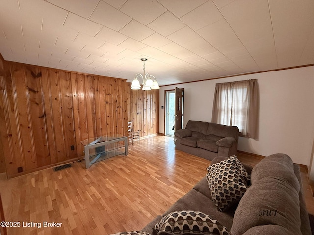 living room with a chandelier, wooden walls, light wood-style flooring, and crown molding